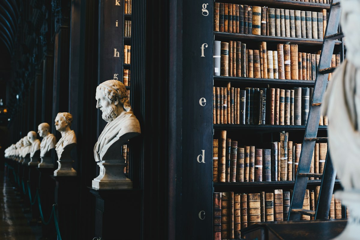 A dark library of leather-bound volumes lined with marble busts